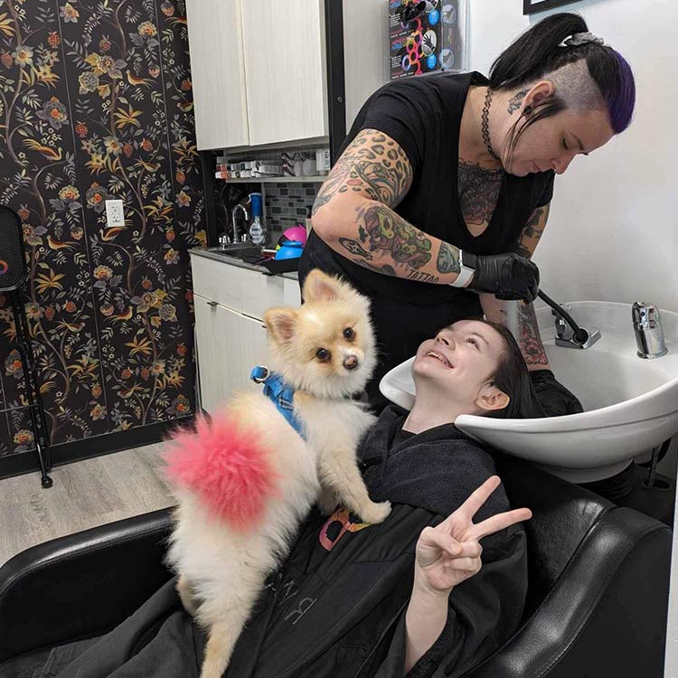 Britt Bishop washing a client's hair with Tut, the salon dog, sitting in the clients lap